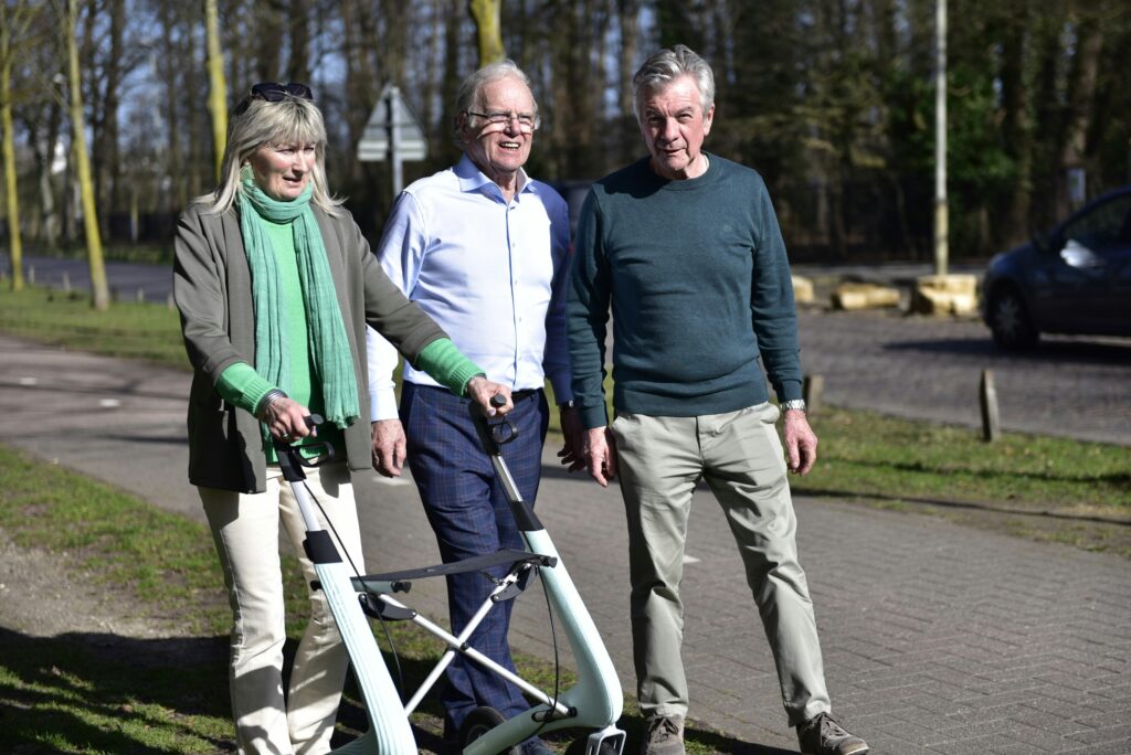 Three active older adults walking outdoors on a paved path, with a woman using a modern rollator, demonstrating the independence maintained through supported living.